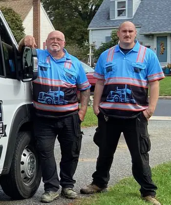 Two men standing next to a truck on the side of the road.